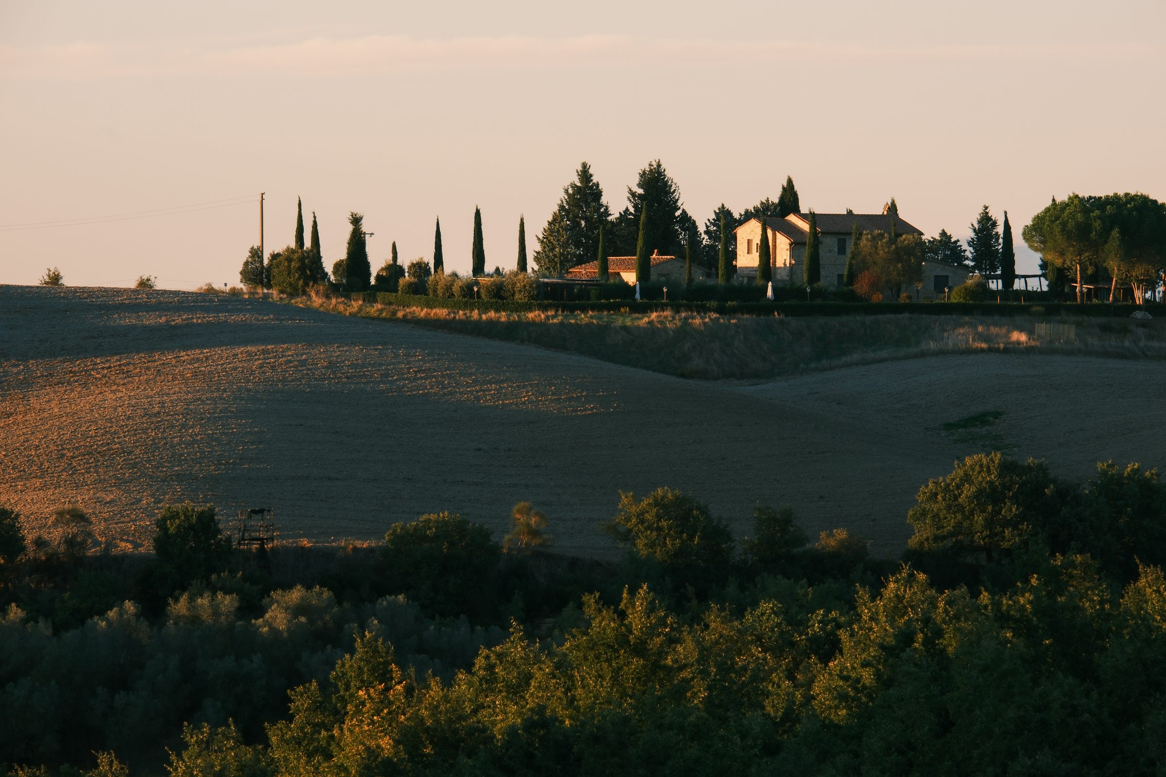 Campagna toscana con campi, alberi e un casale al tramonto